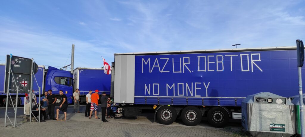 Streikende LKW-Fahrer*innen bei einen blauen LKW mit der Aufschrift MAZUR DEBTOR, NO MONEY